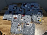 Group view of 12 individually packaged gray Wilson adult baseball pants laid out on wooden surface