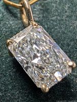 Close-up of emerald-cut diamond in four-prong setting attached to gold bail