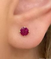 Close-up image of one ruby stud earring being worn on an ear, showing gold four-prong setting and vibrant ruby color.