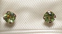 Close-up photo of two round green gemstone earrings set in 10kt gold four-prong settings on a textured cream card.
