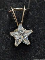 Close-up of a star-shaped clear faceted gemstone set in a 14kt gold prong setting with a V-shaped gold bail on a black fabric background.