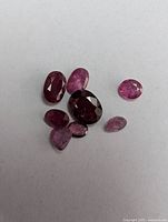 Top-down photo showing seven assorted faceted rubies in red to pink shades on a white background
