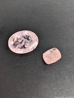 Two light pink morganite gemstones on black background, one oval faceted larger stone and one rectangular smaller stone.