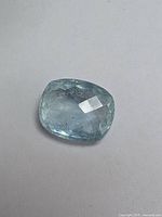 Top view of a light blue cushion cut aquamarine gemstone showing faceting and internal inclusions.