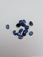 Top view of multiple blue sapphire gemstones scattered on a white background showing various oval and round cuts.