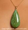 Close-up front view of the teardrop green gemstone pendant showing polished surface, natural color variations, and metal setting loop.