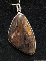 Close-up photo of a genuine gemstone pendant with natural brown, reddish and black swirls set in metal bezel with a top metal loop.