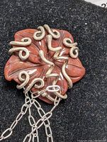 Close-up photo of red carved gemstone pendant with silver swirl accents attached to silver chain on black background.