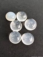 Top-down photo showing six polished round moonstone spheres arranged on a black surface.