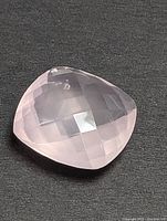 Photo of a faceted cushion cut rose quartz gemstone on a dark background showing color and cut details.