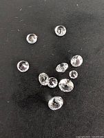 Multiple loose white sapphire gemstones scattered on black fabric, showing size variation and faceting