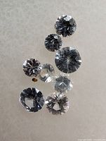 Seven round faceted white sapphire loose gemstones with visible internal inclusions on a light background.