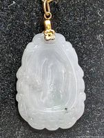 Front view of the translucent light green jade pendant with carved design and gold floral bail.