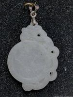 Front view of translucent white jade pendant with circular center and surrounding carved cloud-like shapes with three small holes. Attached silver-tone bail for necklace.