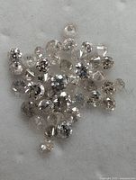 Close-up photo of multiple small natural diamonds loosely displayed on a white surface, showing round brilliant and irregular shapes in various clarity grades.