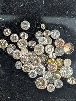 Close-up image showing multiple loose round brilliant cut diamonds on black fabric background, displaying various natural fancy colors including light yellow and brown hues.