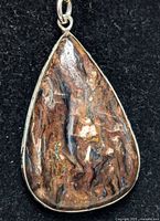 Front view of the natural gemstone pendant with polished brown and tan swirling patterns, set in silver-colored metal frame with bail.