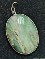 Close-up of oval natural gemstone pendant showing green and brown streaked colors in polished stone with metal bezel setting.
