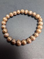 Pearl bracelet laid flat on a black surface showing single strand of imperfect round pearls with ridges and golden color.