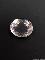 Clear image showing top view of oval faceted rose quartz gemstone with light pink color and faceted surface.