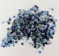 Assorted loose round faceted sapphires in various colors spread on a white surface, showing dark and light blue, greenish and violet stones.