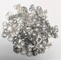 Top view of numerous small silver-colored butterfly clutch earring backs scattered on a white background showing their size, shape and metallic finish.