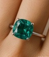 Photo of silver ring with a deep teal-colored cushion-cut stone on a finger showing size and color