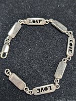Silver bracelet with rectangular plaques engraved 'LOVE' alternated with plain plaques, lobster clasp visible on black background