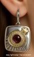 Close-up of a single silver earring showing garnet gemstone and gold-tone stars on textured silver base.