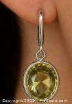 Close-up of earring worn on ear showing bezel set oval lemon quartz gemstone set in silver with lever-back closure.