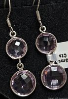 Pair of silver earrings with double round faceted amethyst stones set in bezels, hanging from silver hooks on black background.