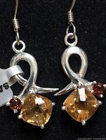 Front view of pair of silver earrings with citrine and garnet stones on black background.