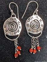 Pair of silver earrings with sun and swirl design, each with three red beads hanging from chains, displayed on black felt.