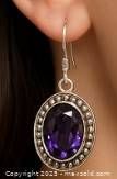 Photo of one silver dangle earring with oval purple amethyst gemstone worn on an ear, showing scale and fit.