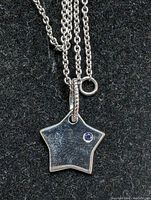 Close-up of star-shaped silver pendant with small blue gemstone and part of silver chain on black background.