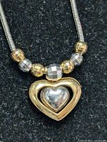 Close-up front view of silver necklace with heart pendant and faceted bead decorations, showing gold and silver tones.