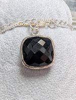 Close-up of square faceted black sapphire pendant in silver bezel with part of silver chain visible.