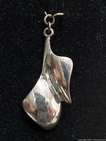 Front view of silver pendant showing organic, flowing shape with subtle hammered texture and loop for attachment.