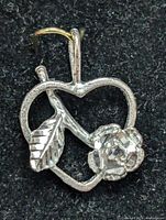 Close-up front view of silver heart pendant with a rose and leaf inside against black background.