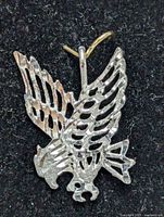 Close-up photo of silver eagle-shaped pendant showing detailed cutout wings, head, and talons on black background.