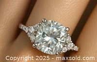 Close-up photo of silver ring on a hand showing the 0.8ct cushion-cut moissanite center stone with smaller side stones and silver band