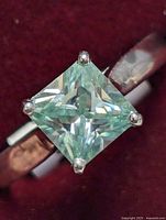 Close-up front view of the square princess cut moissanite held by four silver prongs on band.