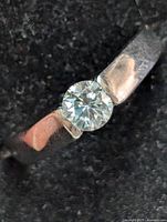 Close-up image of polished silver ring with round moissanite gemstone set in center, showing stone clarity and band finish.