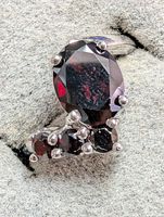 Close-up image of the silver ring showing the large oval garnet center stone with surrounding smaller round garnets.