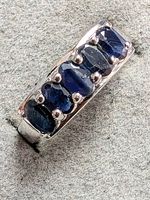 Close-up angled view of silver ring with six oval blue sapphires set in prongs, laying at an angle on grey textured background.