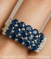 Close-up of silver ring worn on finger showing cluster of blue sapphires and small clear stones on silver setting