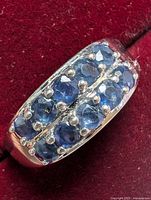 Close-up image showing two rows of blue sapphire stones set in sterling silver ring on red velvet background.