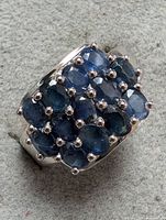 Close-up photo of the silver ring set with multiple oval blue sapphire gemstones arranged in a cluster, showing the top and side angles of the ring.