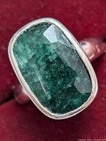 Close-up front view of silver ring with large faceted rectangular emerald set in bezel on smooth silver band.