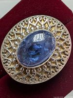 Close-up of silver ring front showing oval cabochon tanzanite and intricate filigree metalwork setting on red velvet background.